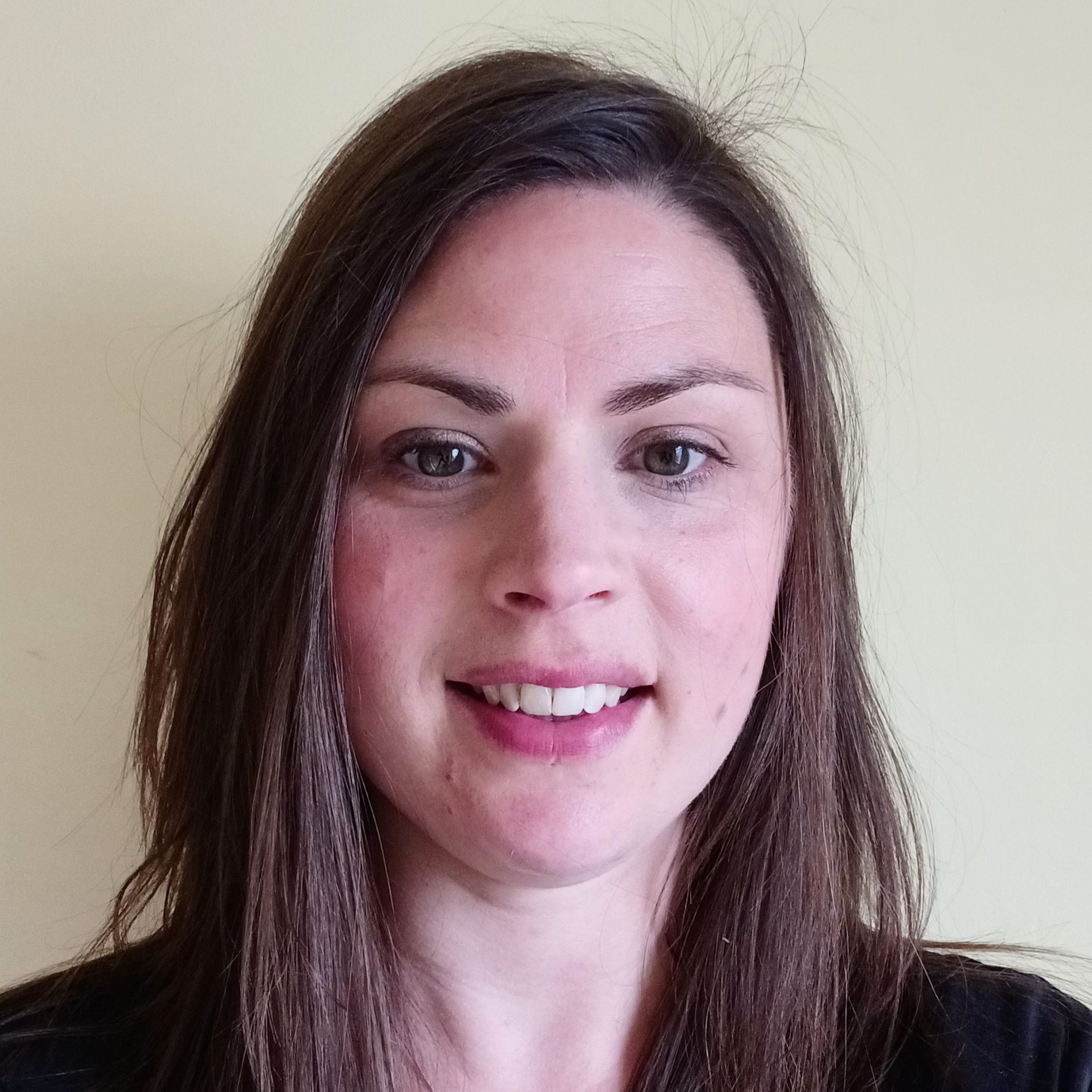 A photo of Jemma Phillips. The photo shows a smiling woman with long straight brown hair and brown eyes, wearing a dark t-shirt.
